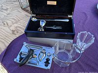 Reed Barton bar tool set with metal jigger, stir stick and other bar tools in a wooden case alongside kitchen tool set on a tray and glass ice bucket and vase nearby on purple cloth.