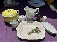 Lot contents on purple background, showing various china and silver-plated items including chamber pot, platter, pitcher, sugar bowl, creamer, salt and pepper shakers, and silver spoons.