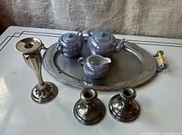 Full view of the lot on tabletop: mid-century modern chrome oval tray with Bakelite handles, a pair of tall silverplate candlesticks, a single shorter silverplate candlestick, and a blue luster Japanese tea set with teapot, sugar bowl, creamer placed inside the tray.
