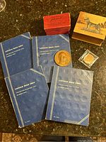 Photo shows four blue Lincoln Head Cent books dated 1909-1940, vintage wooden box with German Shepherd motif on lid, red vintage box for Flinch card game, bronze medal and coin in holder.