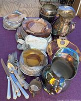 Overall view of the pink depression glass plates, including a bowl with gold overlay, alongside silver plate pitchers and a creamer, and some of the flatware pieces.