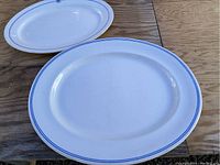 Two oval blue and white antique platters on a wooden surface showing top surfaces and blue striped rims