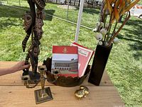Lot consisting of carved wooden statue, brass candelabra, large brass bowl, black pottery vase with silk flowers, gold lacquered paper mache frog, and Chelsea Pensioners books.
