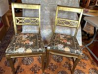 Pair of gold painted side chairs with decorative back panel and floral fabric seats shown side by side