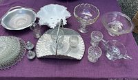 Photo showing the full set of aluminum and glass pieces laid out on a purple cloth, displaying the variety including baskets, bowls, goblets, and plates.