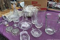 Lot displayed on purple cloth showing large punch bowl, multiple glass cups, decanter, and several small candy dishes and vases.