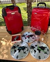 Photo showing two red hard-shell suitcases and the assortment of clocks, tumbler, wine cork stand, and miniature truck arranged on a wooden surface outdoors with trees in the background.