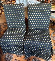 Two side chairs covered in black slip covers with tan circular Chinese pattern, placed on a patterned carpet.