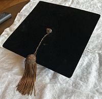 Top view of black velvet mortarboard cap showing square shape and copper tassel with button center