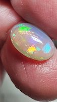 Close-up showing multi-color play of color with dominant green, blue, yellow, and orange flashes on translucent white base in cabochon cut.