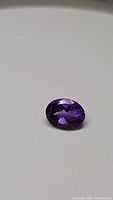 Close-up photo of the 1.85 carat oval cut deep purple Brazilian amethyst gemstone on a white background, showing facets and clarity of the stone.