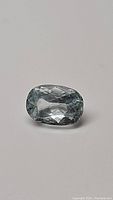 Natural oval cut soft blue aquamarine gemstone, showing facets and clarity under lighting conditions.