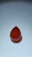 Photo of a deep reddish-orange, faceted carnelian gemstone in briquette shape on a light background