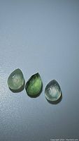 Image showing three polished mossy green prehnite gemstones arranged on a flat surface, two lighter and one dark green with checkerboard cut.