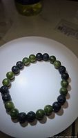 Image of the natural green jade and black lava stone gemstone bracelet laid flat on a white surface showing bead colors and texture.