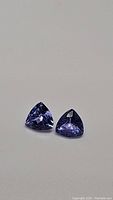 Two trillion cut natural tanzanite gemstones, bright purple-blue color, shown on neutral background