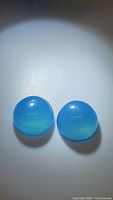 Top view of two round icy blue chalcedony gemstones side by side on a white surface, showing their translucent milky blue appearance and polished domed shape.