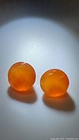 Pair of round cut Mandarin orange carnelian gemstones on white surface under spotlight showing translucent orange color and faceted finish.