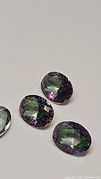 Four oval cut calibrated Mystic Topaz gemstones displaying purple and rainbow coloration on a plain background.