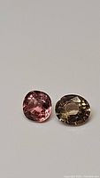 Two natural tourmaline gemstones, one pink cushion cut and one green multicolored oval cut, displayed on white background.