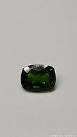 Close-up image of natural chrome diopside gemstone, cushion cut, showing its electric green color and clarity.