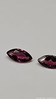 Two marquis cut gemstones placed on a neutral background, showing deep pink purple color and transparent facets.