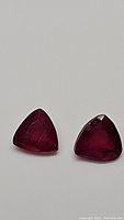 Pair of deep blood red trillion cut rubies lying flat showing faceted top surface and internal features.