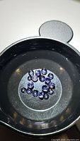 Photo showing entire group of 22 small natural purple iolite stones in a black circular container under light.