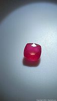 Close-up image of the natural cushion cut ruby gemstone showing deep red color and faceted surface.