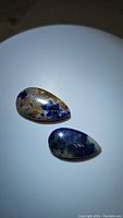 Two pear-shaped sodalite cabochon gemstones, one with mixed brown matrix and blue patches, and one predominantly dark blue with mottled lighter blue areas, polished with smooth cabochon finish.