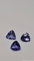 Three natural trillion cut tanzanite gemstones showing blue-purple color and good clarity.