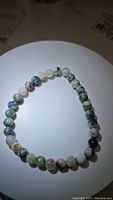 Natural tree agate stretchy bead bracelet laid flat on a white round surface, showcasing the bead colors and patterns.
