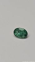 Close-up photo of the oval cut green emerald gemstone showing color and facets.