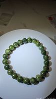 Top view of round polished green jade bead stretchy bracelet highlighting the bead size, color variations, and elastic cord stringing.