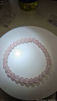 Photo of natural rose quartz stretchy bracelet laid flat on a white circular surface, showing the pale pink translucent beads.