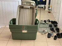 Four stacked Rubbermaid RoughTote storage bins with their lids on top. Light green bins with beige lids visible inside the top bin.