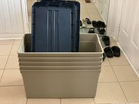 Five stacked gray storage bins with dark gray lids placed on tile floor.