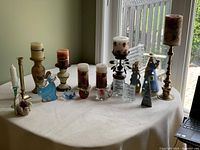 Wide view of all candles and candleholders arranged on a white tablecloth under natural light.