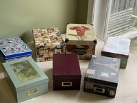 Seven decorative boxes of various designs and sizes arranged on floor near window.