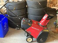 Side view of red Honda snow blower showing auger housing, wheels, and chute