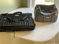 Black Air Express garment bag with multiple compartments and handles on left; Gray and black Voyageur duffle tote bag with handles on right