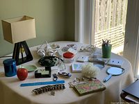 Wide view of table with lamp, power bars, extension cords, small home decor items, ruler, watches, bath sponge, handheld mirror, and more.