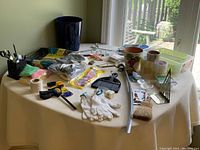 Lot contents including various household and garden items spread on a table with window background
