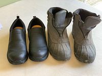 Pair of Dakota Tarantula Work Pro Series black slip-on shoes and Sorel winter boots side by side