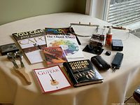 Overview of guitar books, guitar polish spray, 3 Snark tuners, guitar straps, harmonica neck wraps, and Newfie spoons on table.