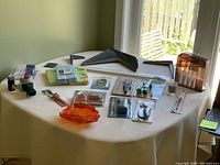 Full view of the mixed lot on round table including metal brackets, decorative glass basket, craft tools, tape dispenser and other household items
