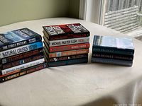 All 15 novels stacked in three piles on a table near a window.