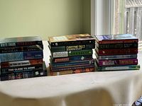 Stack of 19 novels arranged on a white surface, showing a variety of authors and book titles.