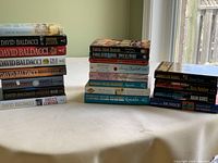 Stack of novels including multiple by David Baldacci, Barbara Taylor Bradford, and James Lee Burke shown on table