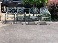 Four metal outdoor chairs lined up outside, showing their matching design and painted finish.